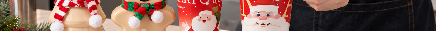 A beverage shop worker checks the fit of a red lid on a Christmas cup beside festive paper cups, novelty bottles, and assorted lids.
